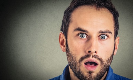 Astonished man. Closeup portrait guy looking surprised in full disbelief isolated on grey wall background. Human emotion facial expressionの写真素材