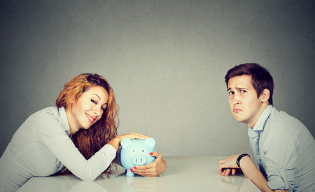 Finances in divorce concept. Happy wife with piggy bank sitting across the table from sad desperate ex husbandの写真素材