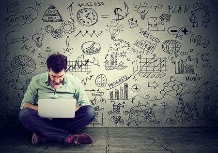 young man working on computer sitting on a floor learning online drawing schemes business plan on a wallの写真素材