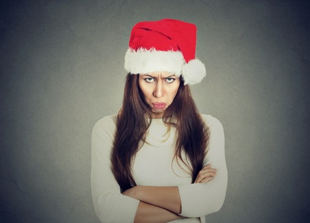 Unhappy upset young woman in red santa claus hat arms crossed folded looking at you isolated on gray background. Negative emotionsの写真素材