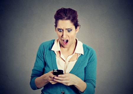 SMS. Shocked anxious scared young girl looking at phone seeing bad news photos with disgusting emotion on face isolated gray background. Human reaction, expressionの写真素材