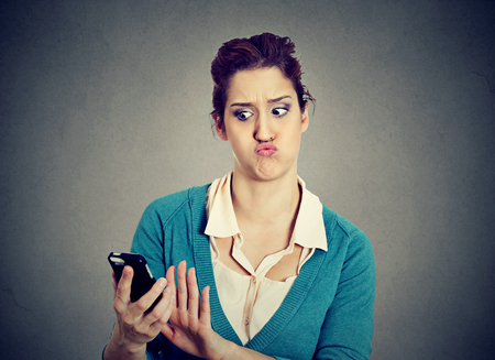 SMS. Shocked anxious scared young girl looking at phone seeing bad news photos with disgusting emotion on face isolated gray background. Human reaction, expressionの写真素材