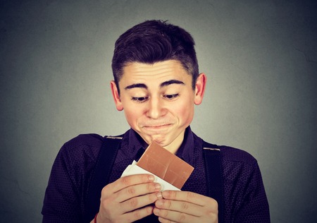 Man tired of diet restrictions craving sweets chocolate. Human face expression emotion. Nutrition concept. Feelings of guiltの写真素材