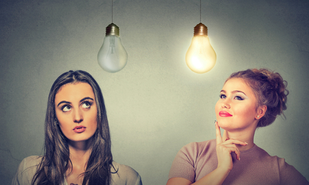 Two women thinking looking up at light bulbs isolated on grey wall background. Human face expressions, emotions, perception. Cognitive skills ability conceptの写真素材