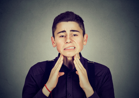 Man with sore throat. Sick young boy having pain touching his neck isolated on gray wall background