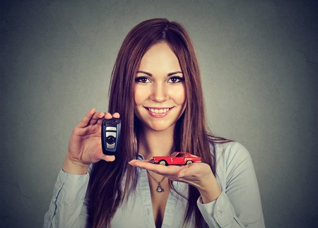 Happy young woman showing model car and remote keys isolated on gray background. Personal transportation purchase conceptの写真素材