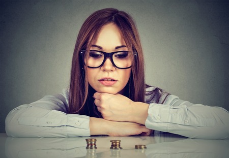 Young ambitious business woman sitting at table looking at growing stack of coins. Financial freedom target success conceptの写真素材