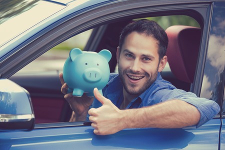 Happy man sitting inside his new car holding piggy bank showing thumbs upの写真素材