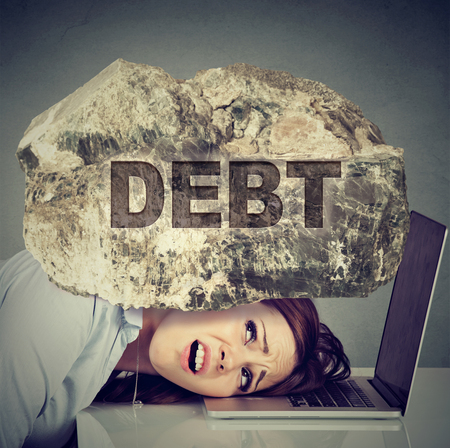 Young desperate business woman with her head squeezed between laptop computer and a rock. Student university education loan debt conceptの写真素材