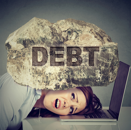 Young desperate business woman with her head squeezed between laptop computer and a rock. Student university education loan debt conceptの素材 [FY31070835186]