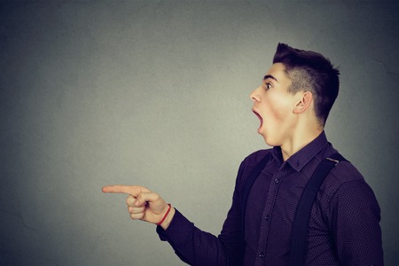 Shocked man pointing finger isolated on gray background with copy space の写真素材
