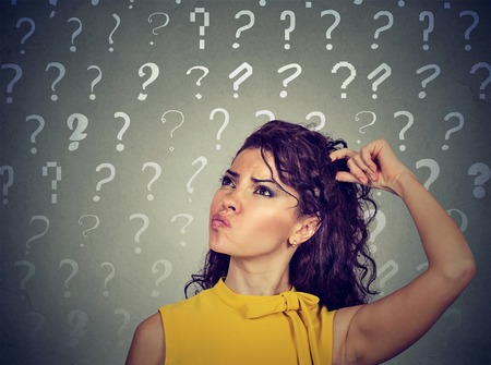 Portrait confused thinking young woman bewildered scratching her head seeks a solution looking up at many question marks isolated on gray background. Human face expressionの写真素材