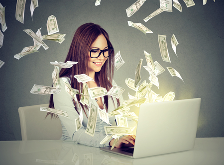 Professional smart young woman using a laptop building online business making money dollar bills cash coming out of computer. Beginner IT entrepreneur success economy concept Professional smart young woman using a laptop building online business making money dollar bills cash coming out of computer. Beginner IT entrepreneur success economy concept