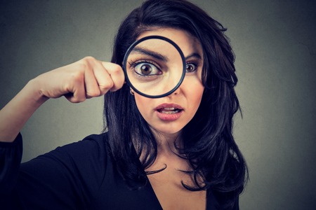 Surprised woman looking through magnifying glass isolated on gray wall background.の写真素材