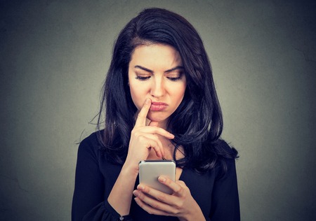 Thoughtful confused woman looking at her smart phone isolated on gray backgroundの写真素材