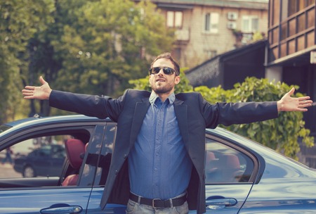 Successful happy young man standing by his new car enjoying summer day