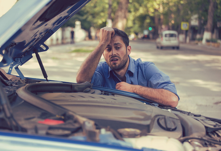 young stressed man having trouble with his broken car looking in frustration at failed engine