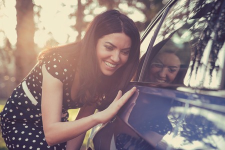 Excited young woman and her new car outdoors with sunlit forest in background.の写真素材
