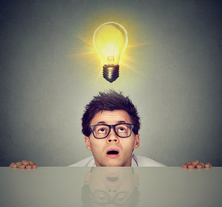 Man coming out from under the table looking up at bright light bulb above headの写真素材