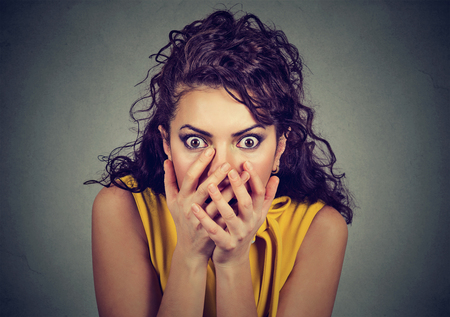 Scared shocked woman with hands over her mouth isolated on gray background  