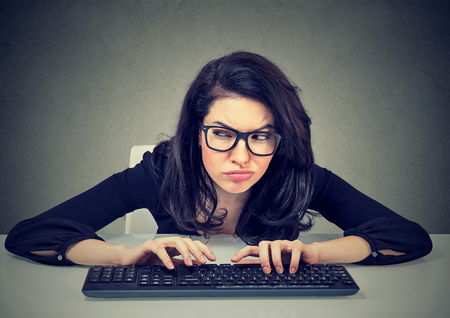 Crazy looking nerdy woman typing on the keyboard wondering what to reply plotting a revengeの写真素材