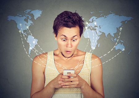 Shocked man looking at his smart phone with world map on a background 