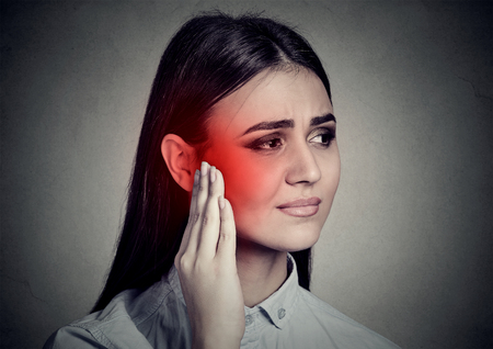 Tinnitus. Closeup sick woman having ear pain touching her temple head isolated on gray wall background の写真素材