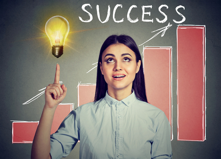 Successful woman looking up at bright idea light bulb with growing success chart on a backgroundの写真素材