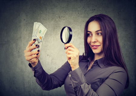 Young woman looking at one hundred dollar bills through magnifying glassの写真素材