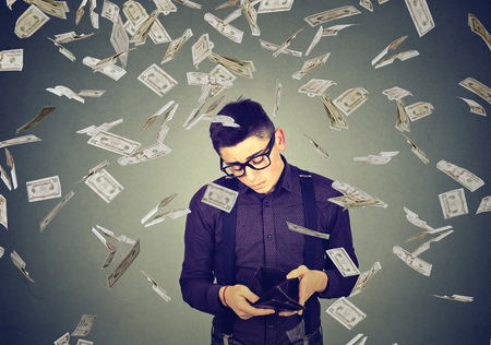 Young sad man looking at his empty wallet under money dollar banknotes rain