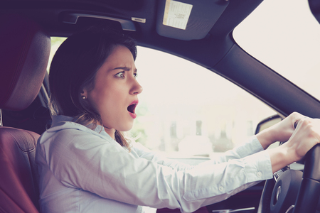 Young woman driving a car shocked about to have traffic accident, side window viewの写真素材