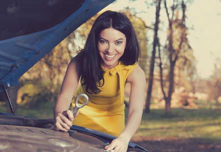 Portrait of a happy woman holding a wrench confidently with her broken down car on a rural park forest backgroundの写真素材
