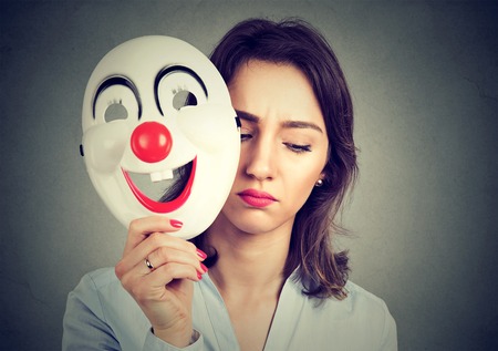 Portrait sad woman taking off happy clown mask isolated on gray wall background. Human emotions feelingsの写真素材