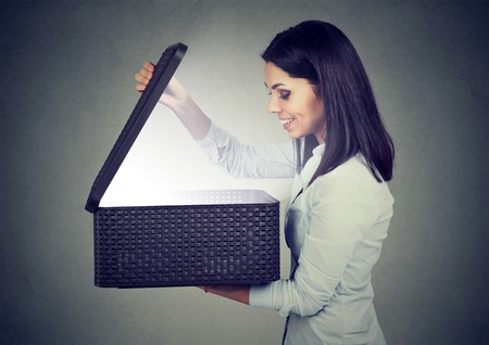 Happy woman opening looking into gift box with bright light coming outの写真素材