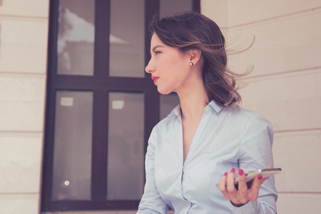 Frustrated annoyed sad woman with mobile phone standing outside apartment condoの写真素材
