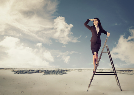 Young businesswoman on a ladder looking faraway in a desertの写真素材