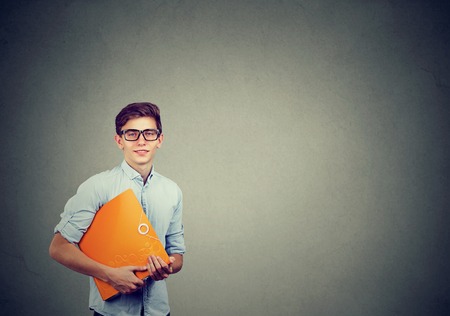 Portrait of young happy smiling man with orange folder isolated on gray background with copy spaceの写真素材