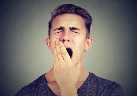 Sleepy young man yawning. Sleep deprivation, burnout, laziness conceptの写真素材