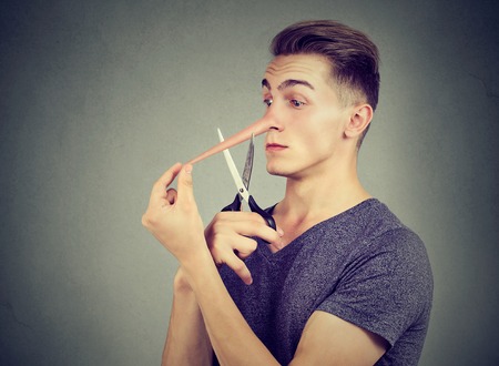 Worried liar man wants to cut his long nose isolated on gray wall background.の写真素材