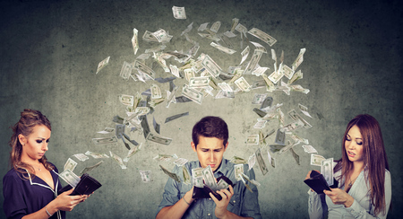 Worried sad man and two women looking at their wallets with money dollar banknotes flying out awayの写真素材