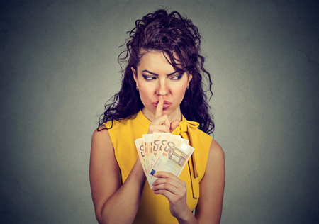 Woman holding pile of euros and asking for silence while practicing corruption.