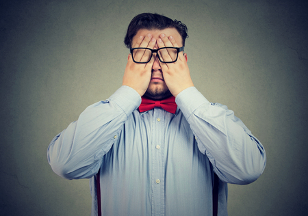 Chunky man in formal clothing and eyeglasses covering eyes with hands looking tired. の写真素材