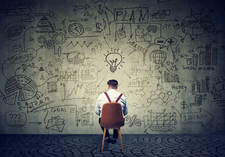 Back view of chunky man sitting in front of wall with strategy and creating plan. の写真素材