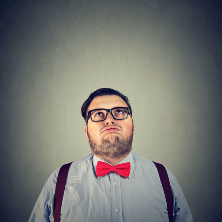 Young chubby man in bow tie looking up in boredom posing on gray background. の写真素材