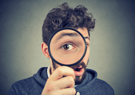 Curious amazed young man looking through a magnifying glassの写真素材