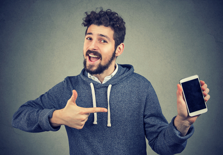 Young cheerful man showing new phone happy with great quality. の写真素材