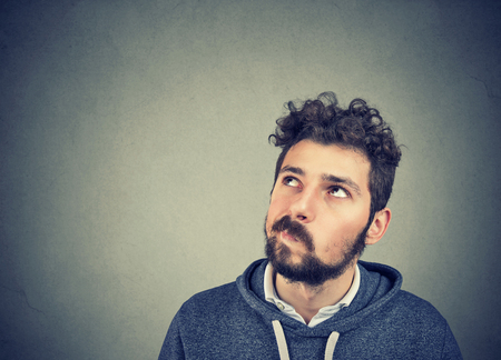 Young bearded man in puzzlement looking up and considering problem in mindfulness. の写真素材
