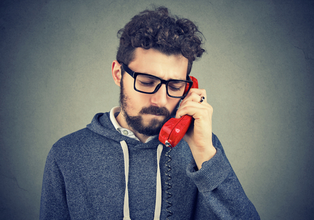 Young bearded man talking on telephone and looking unhappy with heart broken. の写真素材