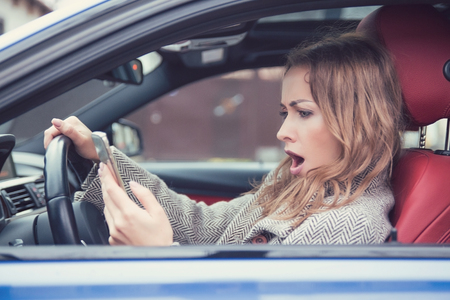 Side view of woman watching smartphone with breaking news while sitting inside of own car. の写真素材