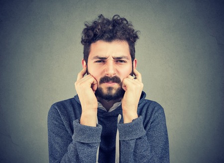 Annoyed man looking grumpy plugging with fingers ears unwilling to listen to anyone. 